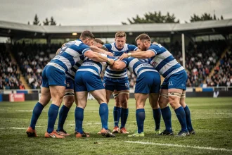 Joueurs de rugby français en cercle d'équipe avant un match de championnat, jerseys bleus et blancs sur pelouse naturelle